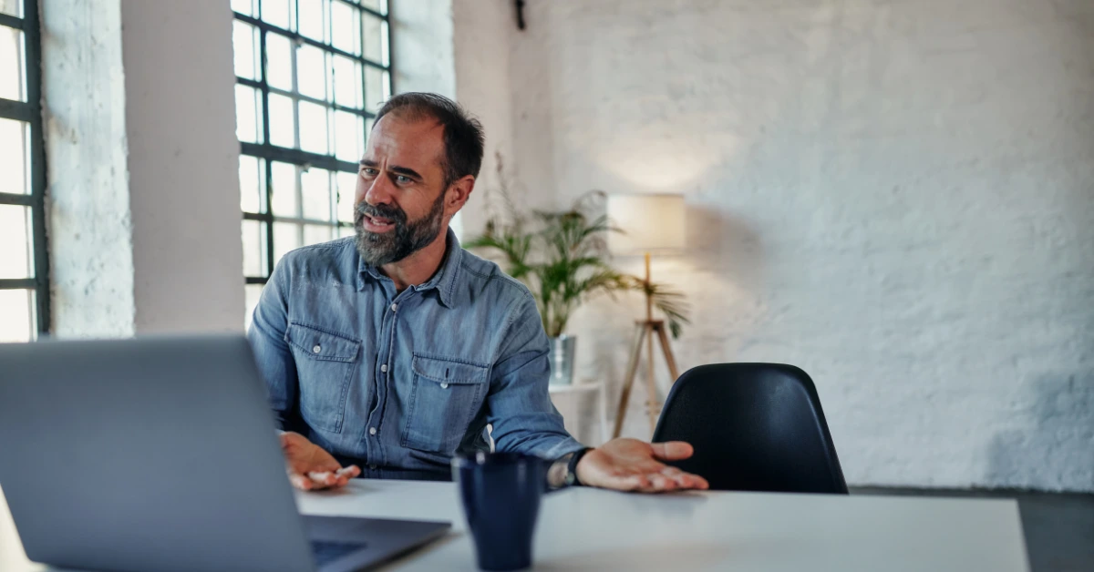 Man sitting in a home office engaged in an online therapy session via laptop, representing virtual counseling and telehealth services.
